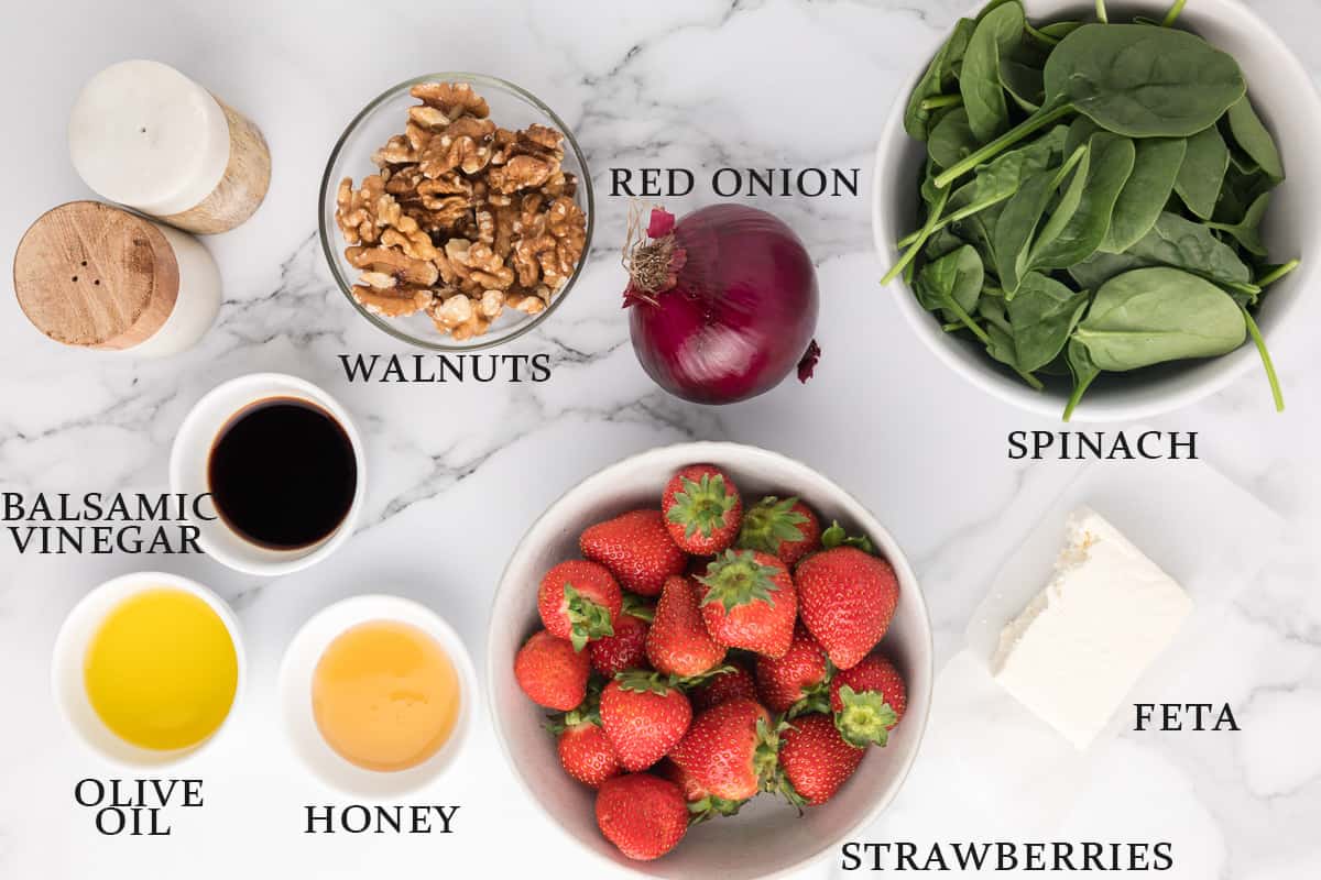 Ingredients to make a strawberry salad on a marble background with text overlay.