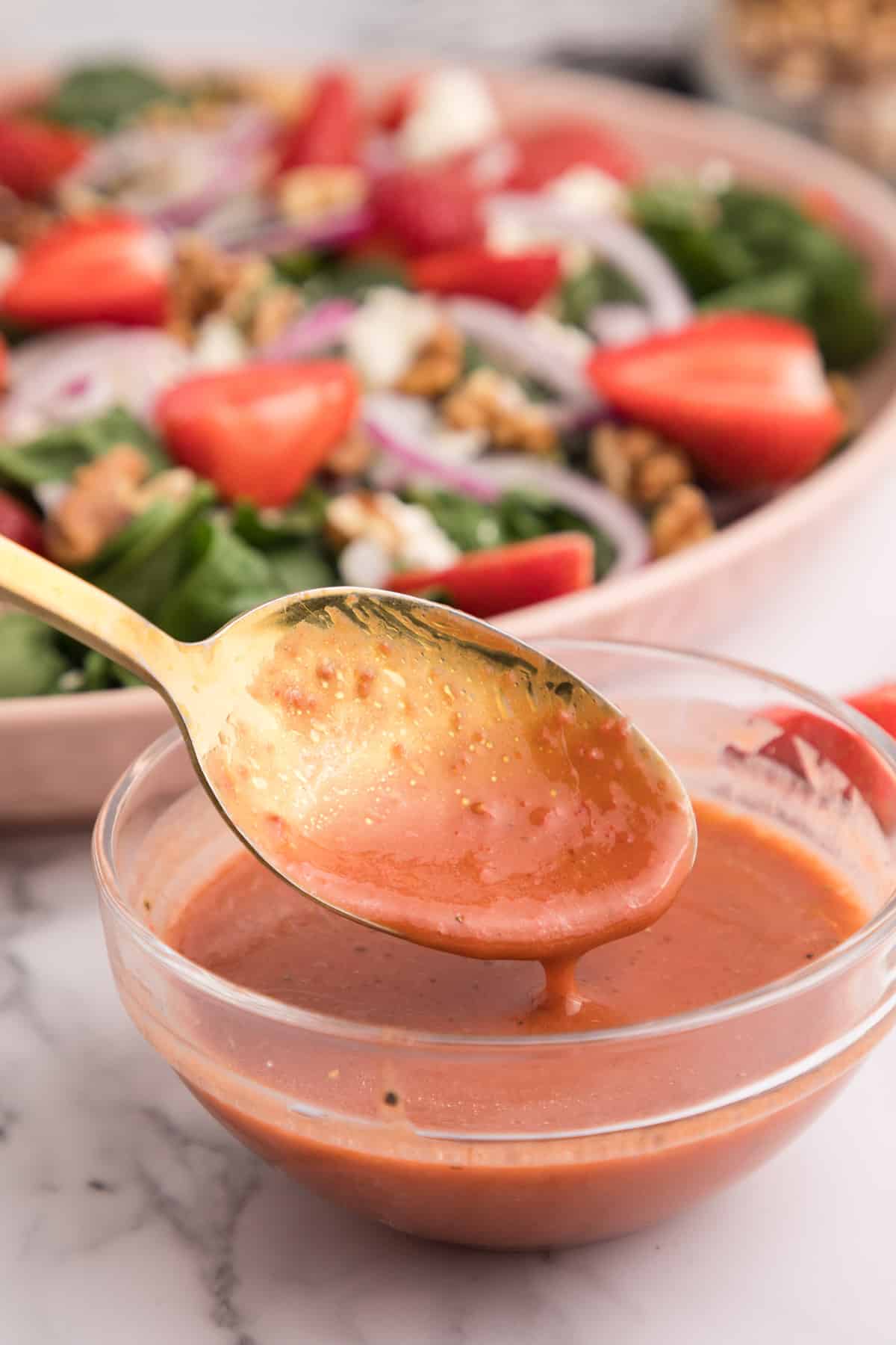 Strawberry balsamic vinaigrette in a glass bowl with a gold spoon lifting some up.