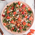 Overhead of a strawberry spinach salad with strawberry dressing on a large pink plate.